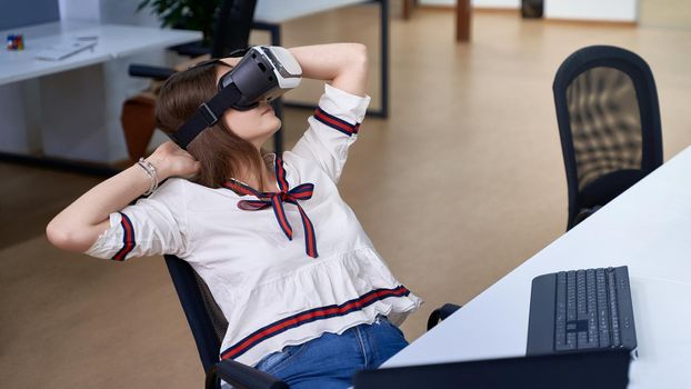 Beautiful young woman working with virtual reality headset in IT office, sitting at desk. Working on a project in software development company or technology startup.