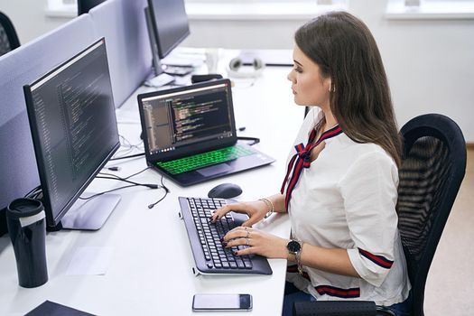 Beautiful young woman working on computer in IT office, sitting at desk and coding, working on a project in software development company or technology startup.