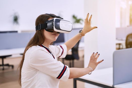 Beautiful young woman working with virtual reality headset in IT office, making gestures. Working on a project in software development company or technology startup.