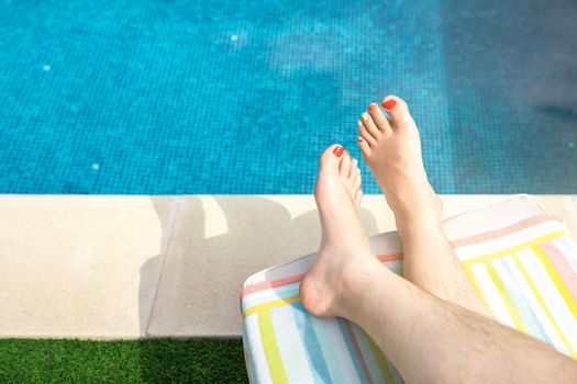 Close-up of the bare feet of a young man lying on a deckchair in a swimming pool. barefoot man with his nails painted in LGTBIQ colours. concept of travel and leisure. natural sunlight, outside, garden with swimming pool.