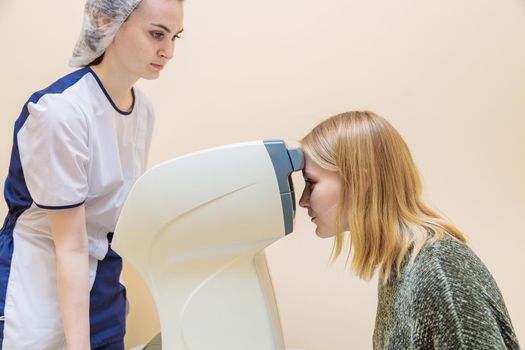 A girl optometrist examines the eyes of a patient using special modern equipment.