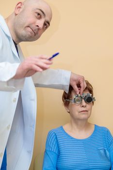 A male optometrist checks the eyesight of an adult woman with a trial frame.