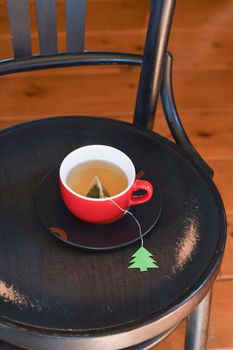 A red cup with tea is wrapped in a warm Christmas sweater, a tea bag label in the form of a green Christmas tree. High quality photo