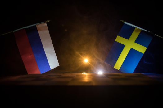 Flags of Sweden and Russia on dark background. Conceptual image of war between Russia and Sweden using national flags . Selective focus