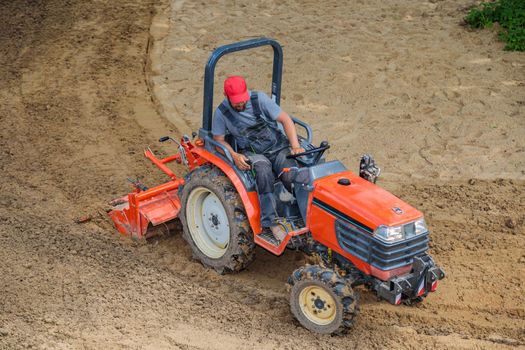 A farmer on a mini tractor loosens the soil for the lawn. Land cultivation, surface leveling.