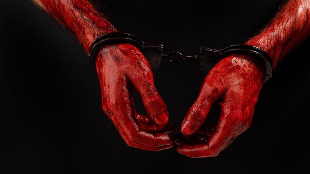 Close-up of male bloody handcuffed hands on a black background