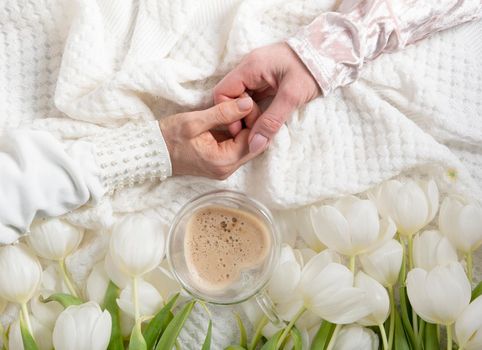 hands of two women holding a heart-shaped cup with cappuccino on two sides, female friendship, flat lay with white tulips, mother's day, valentine's day,