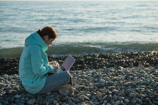 Happy caucasian woman working on a laptop while sitting on a pebble beach