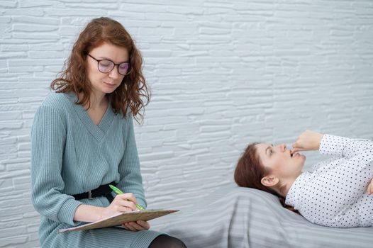 A caucasian woman lies on a couch and expresses her feelings, while a psychologist makes notes on a tablet