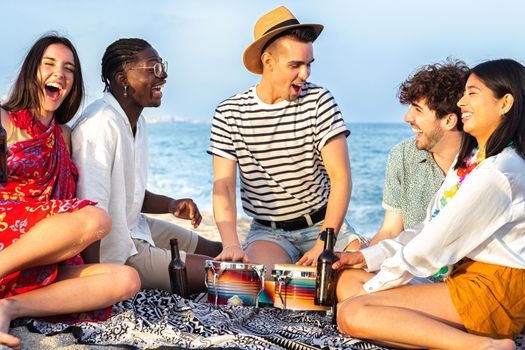 Group of multiracial friends having fun at the beach, laughing out loud, playing bongos and drinking beer together. Vacation and friendship concept.