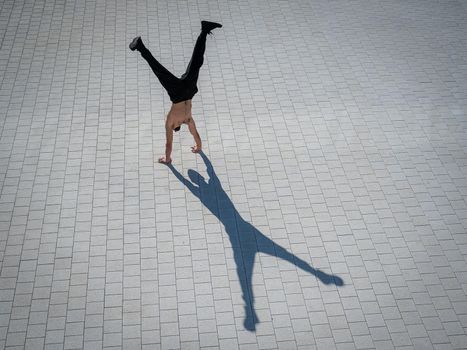 Shirtless man walks on his hands outdoors. View from above