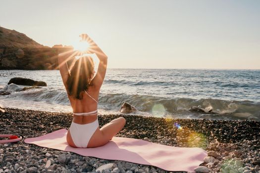 Young woman in swimsuit with long hair practicing stretching outdoors on yoga mat by the sea on a sunny day. Women's yoga fitness pilates routine. Healthy lifestyle, harmony and meditation concept.