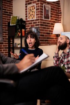 Male psychologist taking notes on paper at couple therapy with angry partners, talking about relationship issues. Doing psychoanalysis with married people, giving counseling advice.