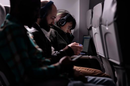 Multiethnic group of passengers flying abroad by airplane jet, using modern devices during international plane transportation. Travelling in economy class with airways flight trip.