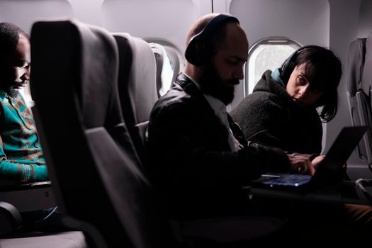 Female passenger looking at man during airplane flight, using laptop online on aerial transportation. Group of tourists travelling by plane on international airline service, aviation jet.