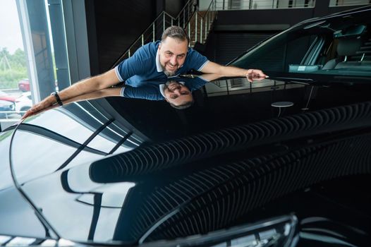 Happy caucasian man hugging the hood of his new car in a car dealership