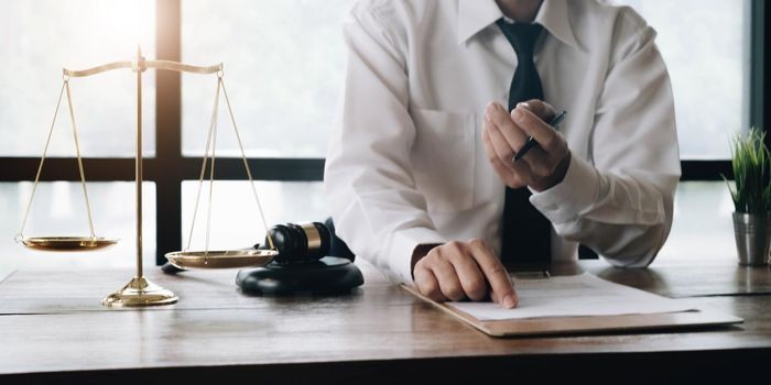 Businessman and lawyers discussing contract papers with brass scale on wooden desk in office. Law, legal services, advice, Justice and real estate concept..