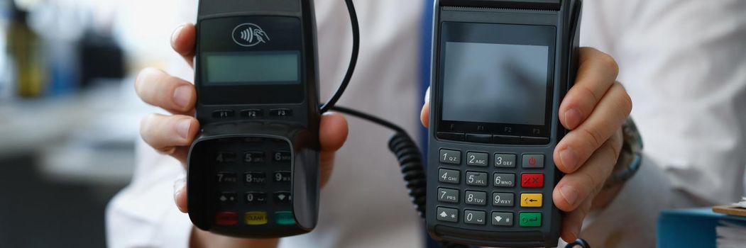 Close-up of man hold different models of credit card reader machines for cashless pay. Empty screen for total cost. Modern technology, development concept