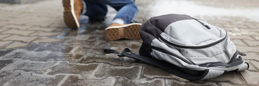 Low angle of man get up from ground after falling on slippery asphalt in winter. Backpack with personal things on surface. Injury, weather, trauma concept