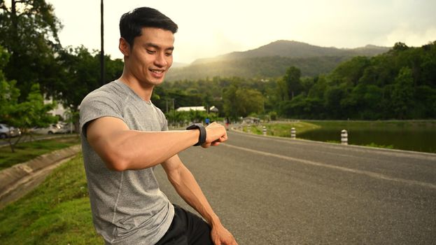 Athletic man resting and checking fitness results on smartwatch. Healthy lifestyle, workout and wellness concept.