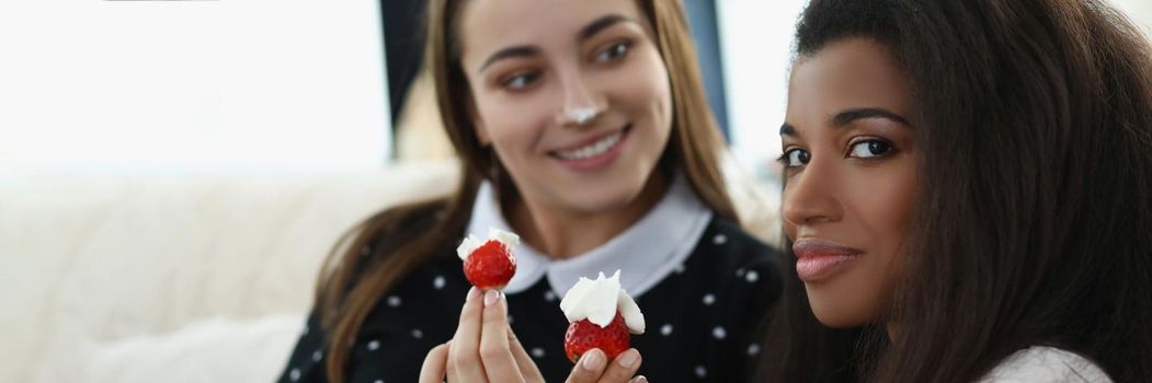 Portrait of smiling pretty women eating tasty fresh strawberry fruit covered with whipped cream. Romantic date at home, best friends. Lgbt, love concept