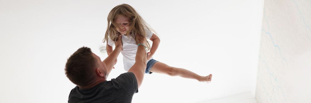 Portrait of father throws child in air and play with kid after work. Happy and healthy relationship in family. Parenthood, childhood, quality time concept