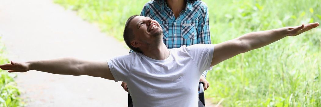 Portrait of disabled man sit in wheelchair, wife drive him behind. Happy and smiling middle aged guy in good mood fly. Happiness, appreciate life concept