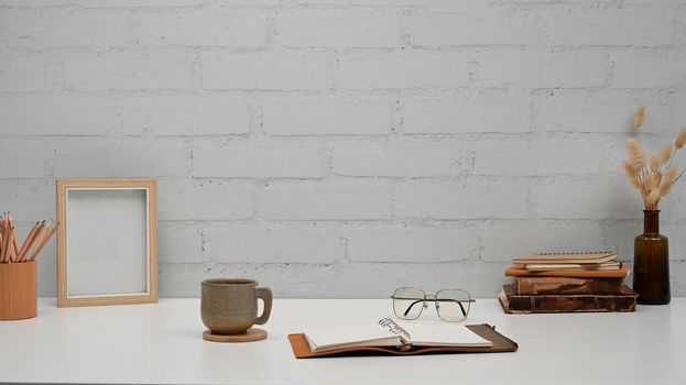 Open book, eyeglasses, picture frame and pencil holder on white table. Copy space for your text.