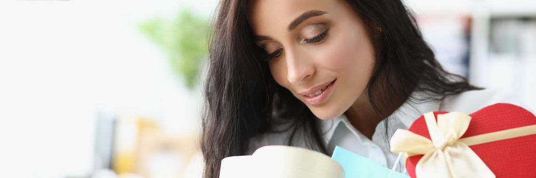 Portrait of brunette female open festive box and search for gift inside, curious look. Present for birthday, anniversary or any event. Surprise concept