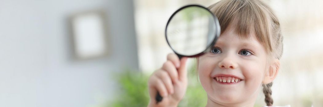 Portrait of pretty little child hold magnifying glass and explore world through it. Smiling happy kid investigate items. Vision, explore, childhood concept