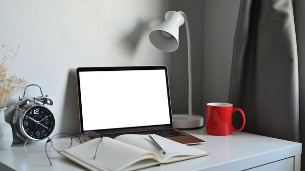 Computer laptop, notebook, coffee cup and lamp on white table.