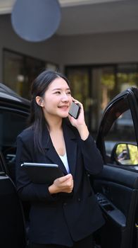 Confident businesswoman standing near her car and talking on mobile phone.