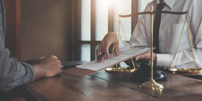 Businessman and lawyers discussing contract papers with brass scale on wooden desk in office. Law, legal services, advice, Justice concept..