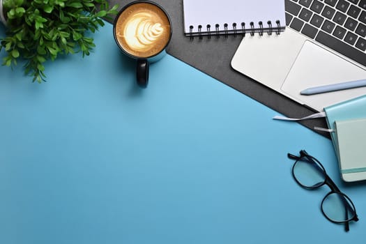 Top view coffee cup, glasses, notebook and computer laptop on blue background.