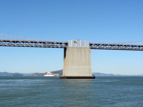 Center of San Francisco side of Bay bridge with a large cargo ship in the distance on a clear day.