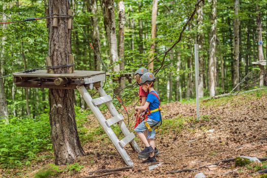 Two boys in a helmet, healthy teenager school boy enjoying activity in a climbing adventure park on a summer day.