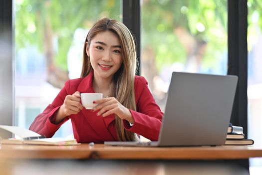 Beautiful businesswoman sitting in front of computer laptop and drinking coffee in the morning.