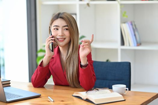 Confident businesswoman talking on mobile phone while sitting in modern workplace.