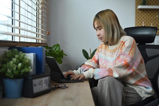 Side view female freelancer working at home with computer tablet.