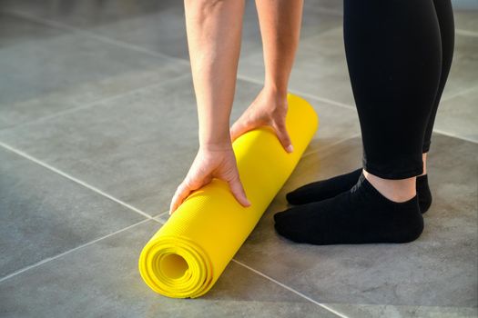 Girl is preparing to unwrap yellow roll of sports mat for yoga. Hands are lying on mat, close-up. Concept of healthy lifestyle.