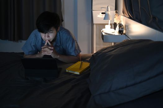 Man sitting in bedroom and using computer tablet at late night.