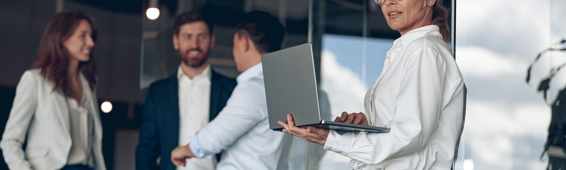 businesswoman at office with group of colleagues on background, working on laptop. Teamwork concept