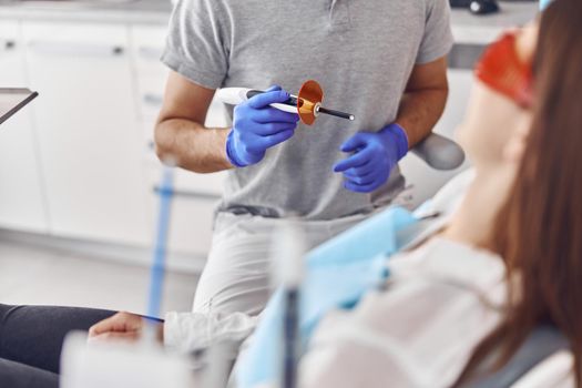 Professional male doctor uses ultraviolet lamp after making a filling on a tooth for joyful happy caucasian woman in modern dental cabinet