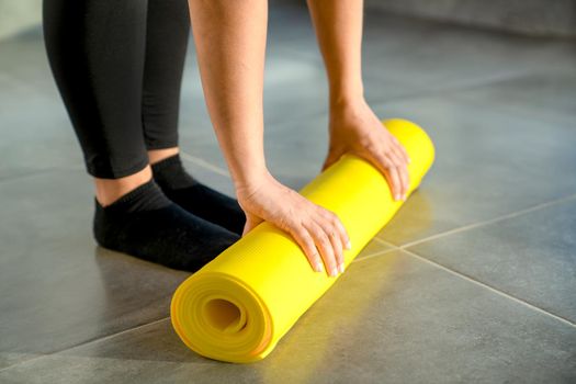 Woman is preparing to unwrap yellow roll of sports mat for fitness. Hands lie on mat, close-up. Concept of healthy lifestyle.