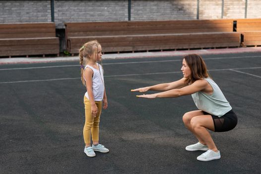 Mother and daughter go in for sports outdoors. Caucasian woman and little girl are engaged in fitness at the stadium