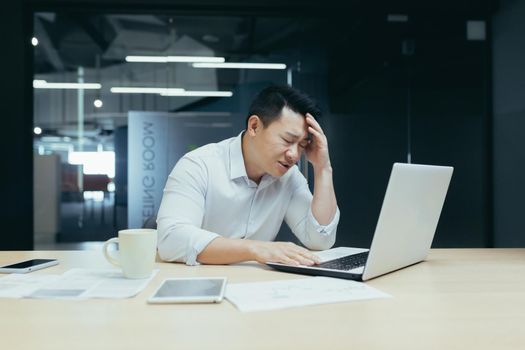 Businessman desperation, asian man working in office, looking at laptop screen, screaming in grief, got bad news