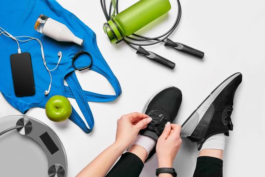 Overhead view of woman hands tying shoes with sport equipments on white background. Top view. Still life. Sports shoes, Fitness concept