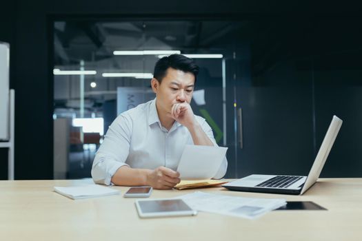 Stressed young asian businessman working from office report annoyed with low sales. Nervous boss see c mistake incorrect information in paper document