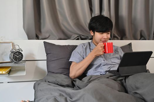 Young man drinking coffee and surfing internet with digital tablet in the morning.