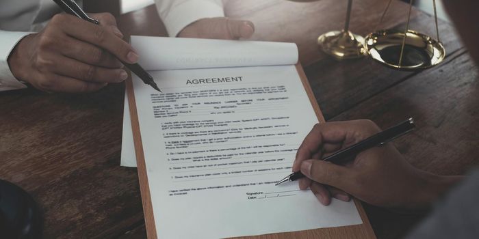 Business and lawyers discussing contract papers with brass scale on desk in office. Law, legal services, advice, justice and law concept picture with film grain effect.